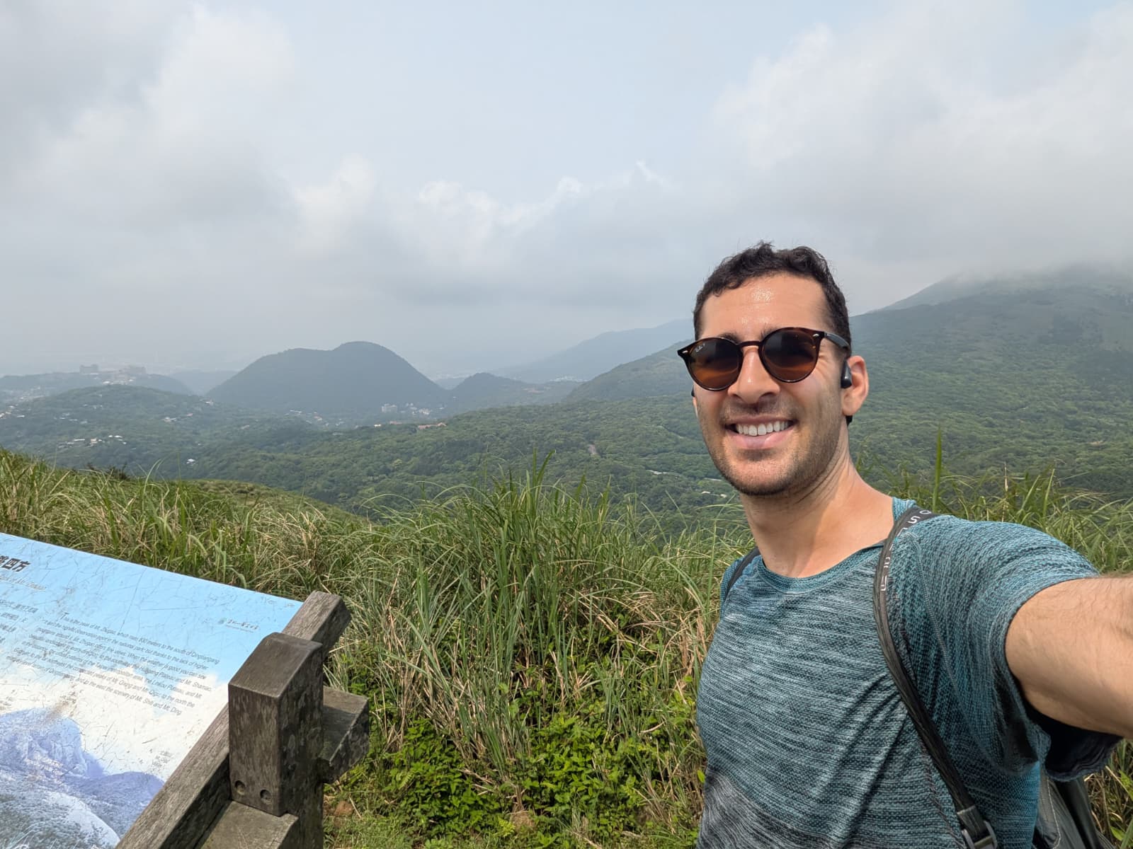 Tyler on a hike above Taipei with green hills and a cloudy sky in the background.